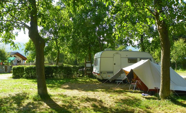 Roulotte e tenda su un prato verde tra alberi.