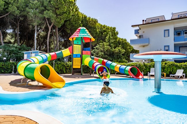 Una piscina con scivoli d'acqua colorati e un bambino che gioca nell'acqua.