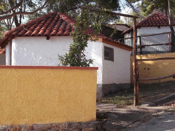 Edifici bianchi con tetti in tegole rosse e muretto giallo, circondati da vegetazione.