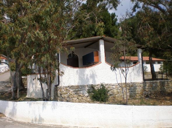Casa bianca con tetto spiovente, all'esterno alberi e muro in pietra.