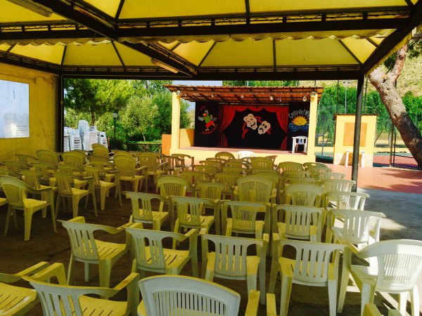 Sedie di plastica e palco teatrale all'aperto.