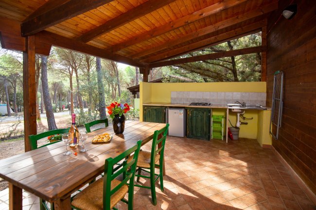 Veranda con tavolo e sedie verdi, vista su cucina esterna.