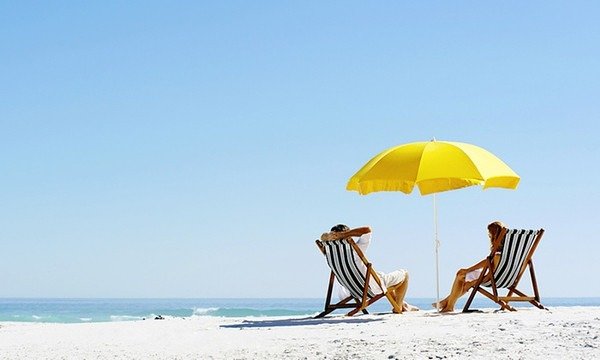 Due persone su sedie a sdraio sotto un ombrellone giallo in spiaggia.