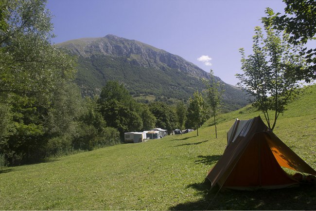 Tenda su prato verde, montagna sullo sfondo.