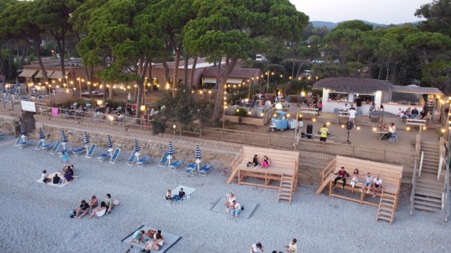 Spiaggia allestita con tavolini e luci.