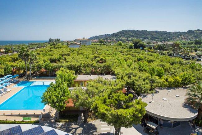 Vista di una piscina circondata da alberi con colline e mare sullo sfondo.