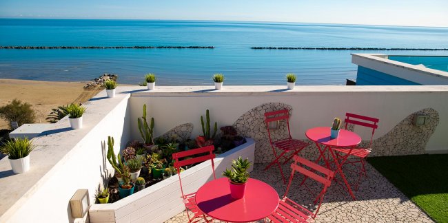 Tavoli e sedie rosse su una terrazza vista mare.