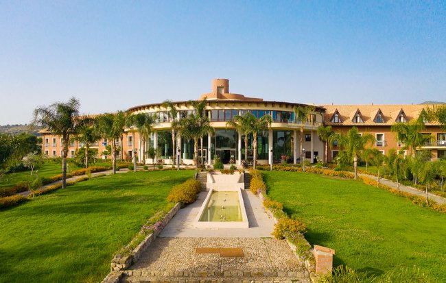 Ampio edificio circondato da prati e palme.