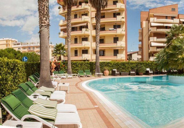 Piscina circondata da edifici e lettini, cielo sereno.