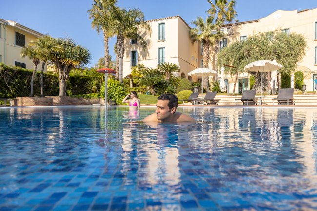 Persone nuotano in piscina all'aperto con palme.