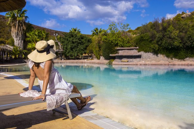 Persona in abito bianco e cappello a falda larga vicino a una piscina.