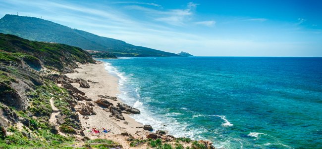 Spiaggia sabbiosa con mare turchese e colline in lontananza.