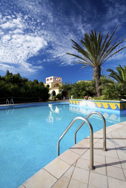 Grande piscina con palme sotto cielo blu.