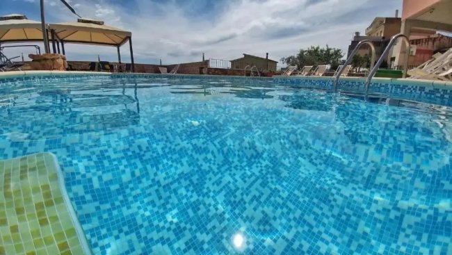 Piscina azzurra con cielo nuvoloso e lettini sullo sfondo.