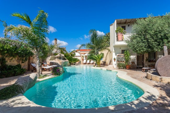 Piscina esterna con palme e cielo blu.