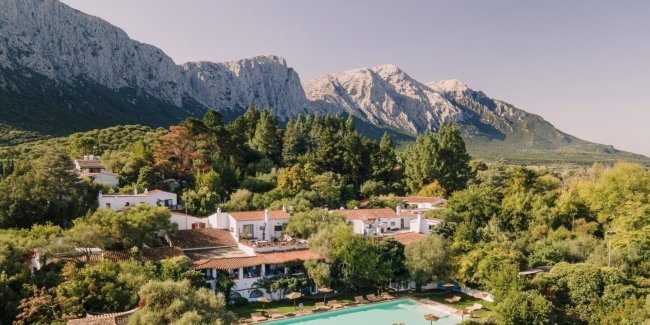 Vista aerea di un complesso con piscina e montagne sullo sfondo.