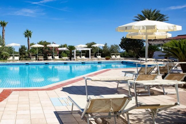 Piscina con sdraio e ombrelloni bianchi sotto un cielo blu.