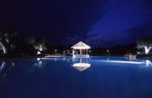 Piscina illuminata di notte con gazebo centrale e cielo scuro.