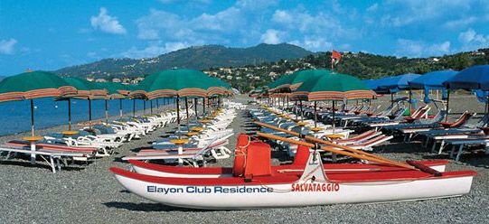 Spiaggia con sdraio, ombrelloni verdi e barca da salvataggio.
