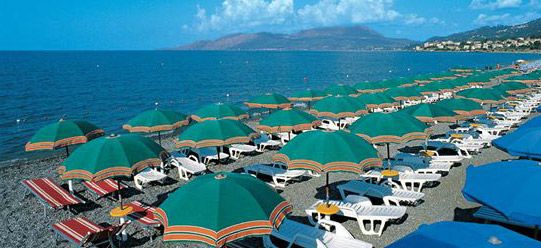 Spiaggia con ombrelloni verdi e lettini bianchi, mare calmo sullo sfondo.
