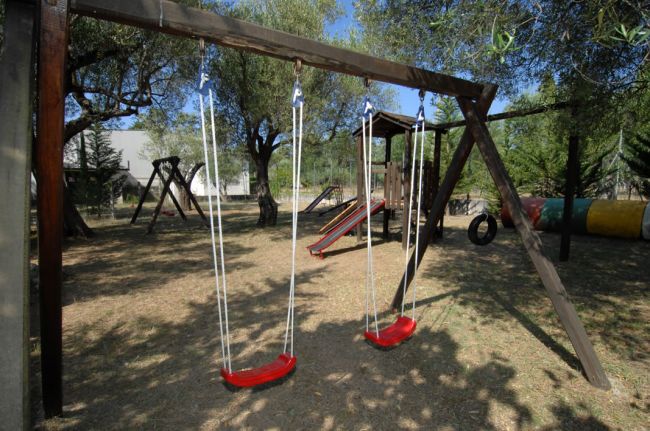 Altalene rosse e scivolo in un parco giochi all'aperto con alberi.