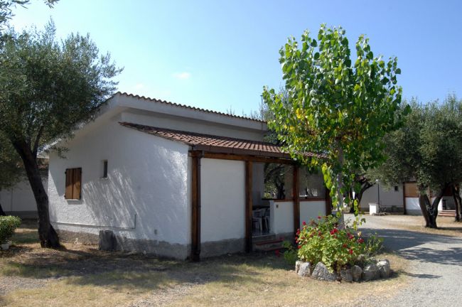 Una piccola casa bianca con tetto in legno, circondata da alberi e fiori.