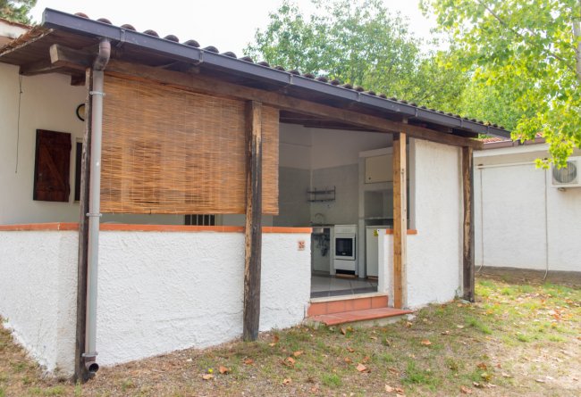 Una piccola casa bianca con patio e stuoia in bambù davanti alla cucina aperta.