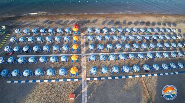Vista aerea di una spiaggia con file ordinate di ombrelloni blu e gialli.