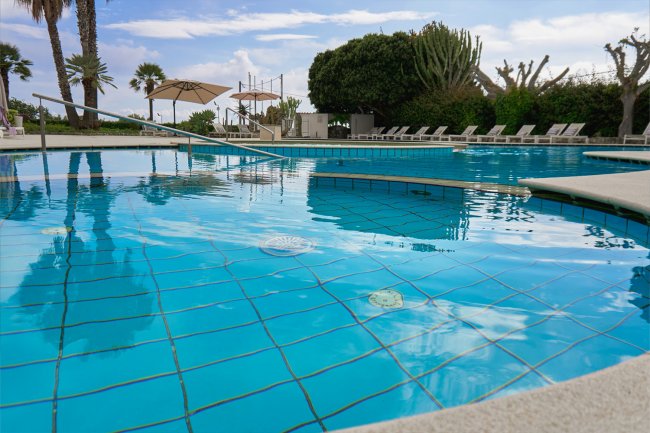 Piscina blu con lettini e ombrelloni.