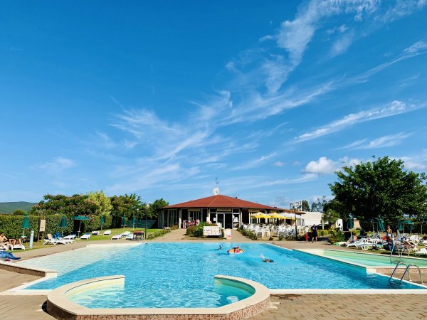 Ampia piscina con bagnanti e un edificio sullo sfondo.