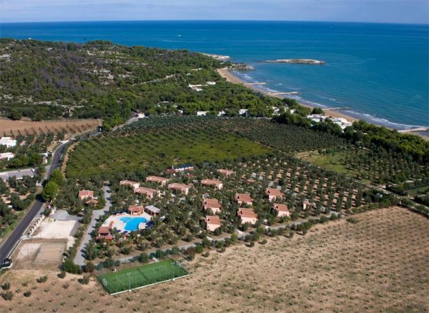 Veduta aerea di un complesso residenziale con piscina, campi e spiaggia nelle vicinanze.