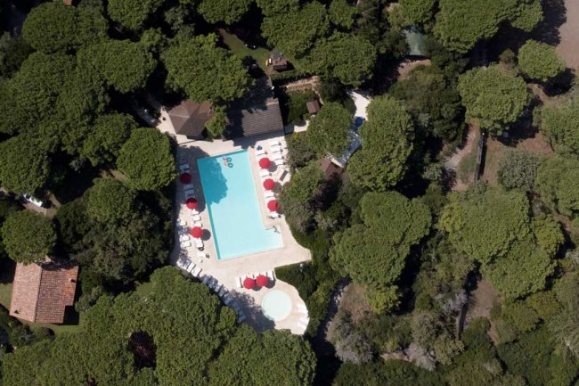 Vista aerea su piscina e ombrelloni rossi, tra alberi verdi.