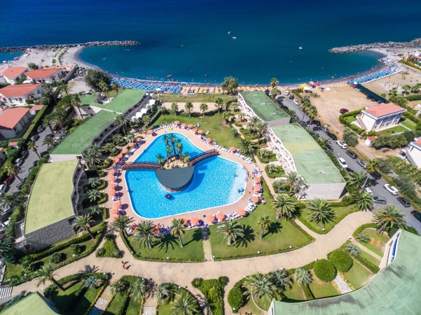 Vista aerea di un complesso con piscina a forma irregolare vicino al mare.