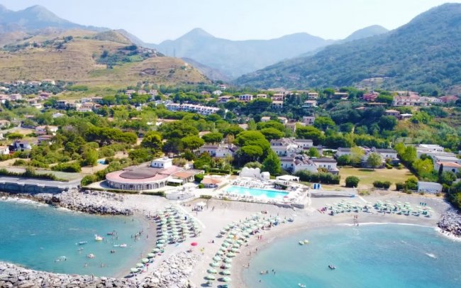 Vista aerea di una spiaggia con ombrelloni e colline sullo sfondo.