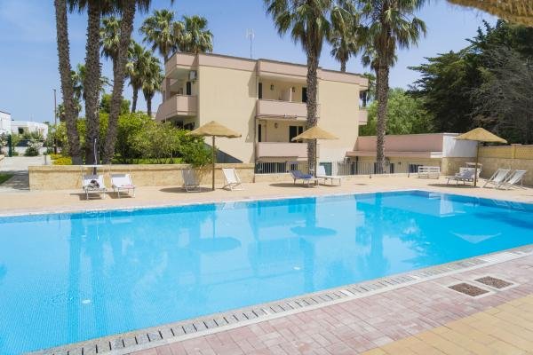 Piscina all'aperto circondata da palme e lettini prendisole.