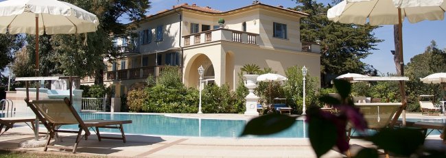 Piscina con lettini e ombrelloni, grande villa sullo sfondo.