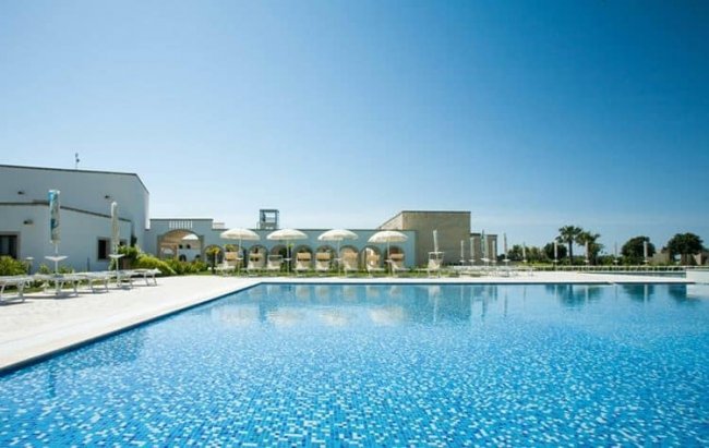 Piscina con piastrelle blu e ombrelloni bianchi.