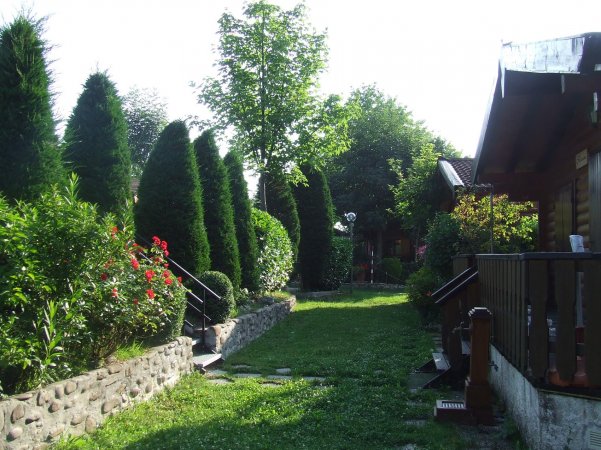 Giardino con siepi e vialetto tra casette di legno.