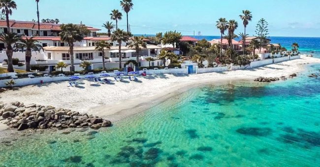 Spiaggia con ombrelloni, ville e mare cristallino.