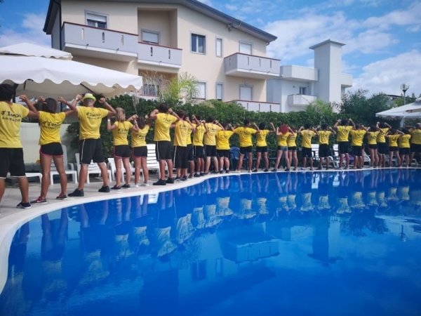 Gruppo in fila con magliette gialle accanto a una piscina.