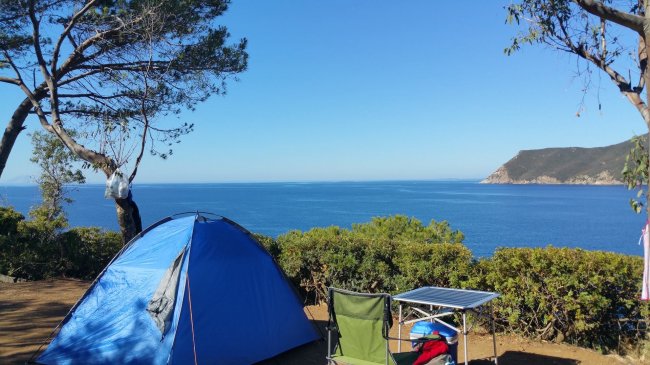 Tenda blu e sedie da campeggio con vista su mare e scogli.