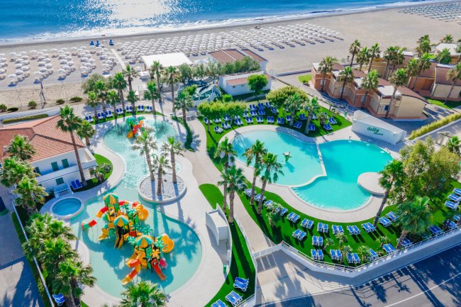 Complesso di piscine vicino a una spiaggia, con palme e giochi d'acqua colorati.