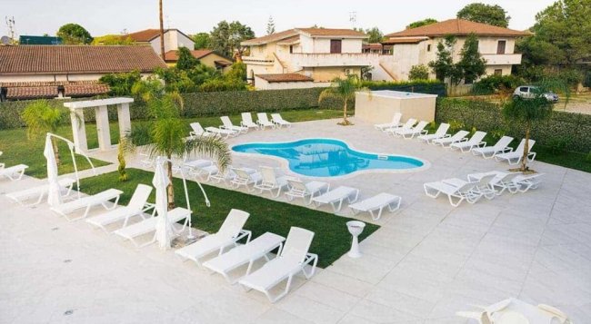 Piscina a forma di fagiolo con lettini bianchi attorno.