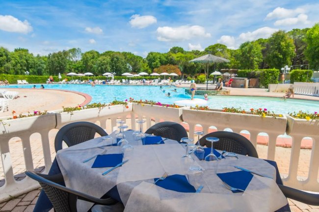 Tavolo apparecchiato vicino a una piscina con sedie e ombrelloni.