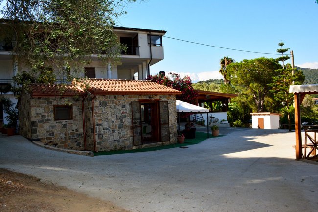 Edificio di pietra con tetto in tegole e piante attorno.