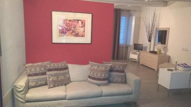 Soggiorno con divano, cuscini e parete rossa.