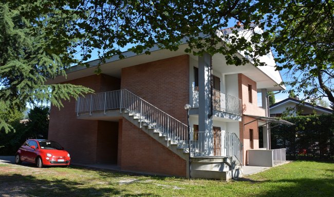 Casa a due piani con scale esterne e auto rossa.