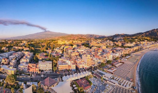 Vista aerea di una città costiera con un vulcano sullo sfondo.