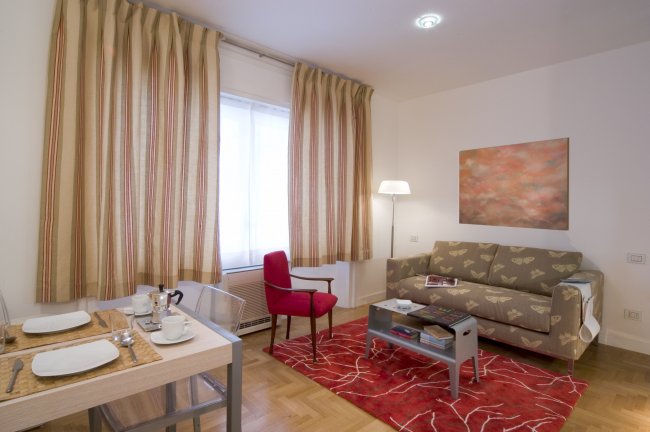 Salotto accogliente con divano, tende e tappeto rosso.