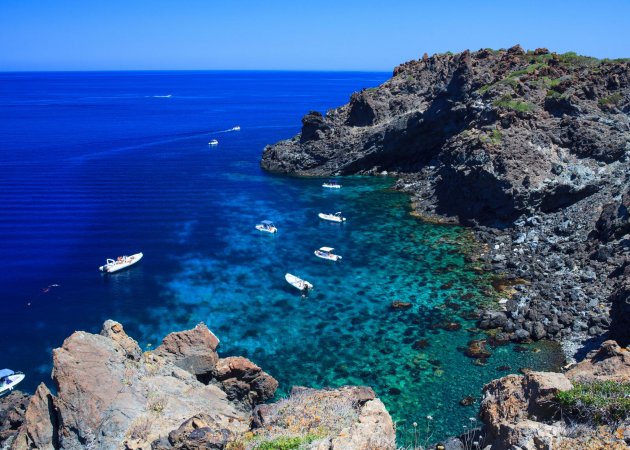 Baia rocciosa con barche e acqua blu.